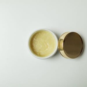 Top view of an open skincare cream jar with a gold lid on a white background for beauty and skincare concepts.